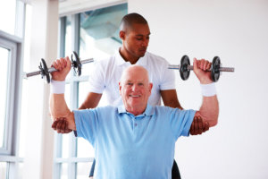personal trainer spots an elderly man as he performs presses with dumbbells.